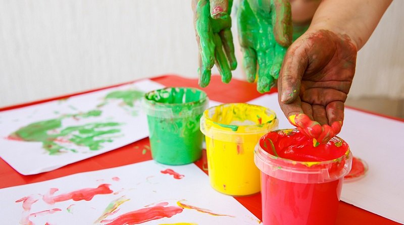 Children dipping fingers in washable, non-toxic finger paints.