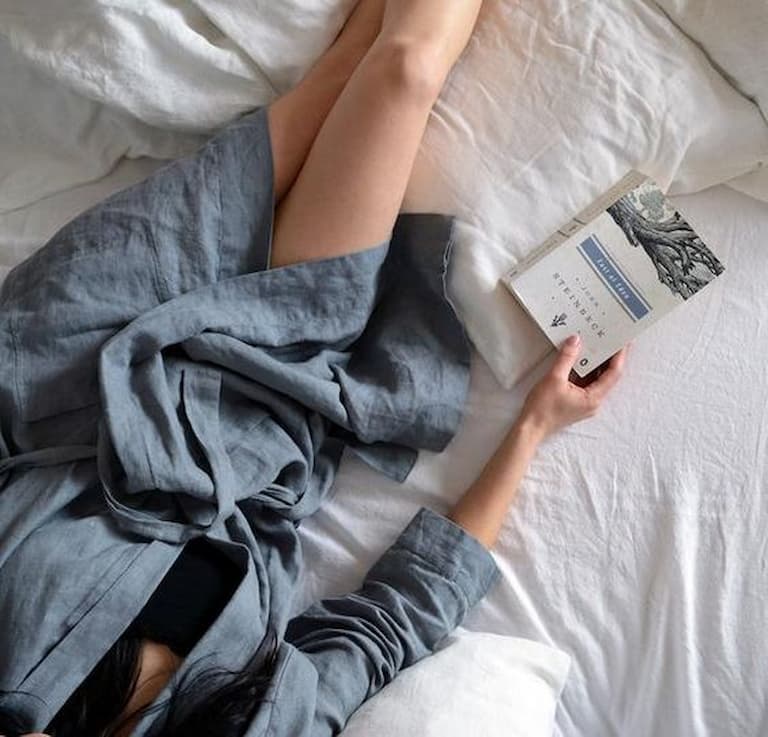 Girl laying in bed reading a book and wearing a blue bathrobe