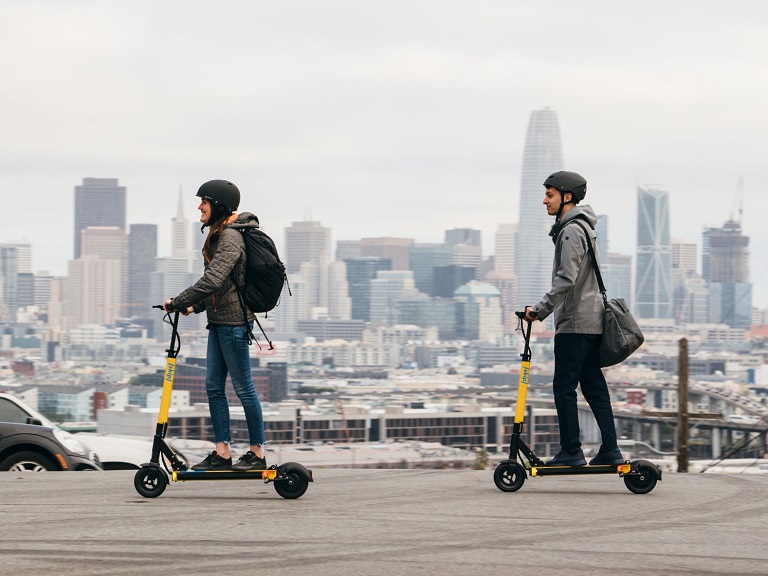 two people riding scooters on the street