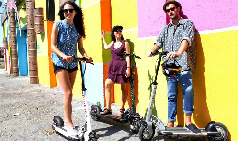 three people standing on scooters with awesome colourful background