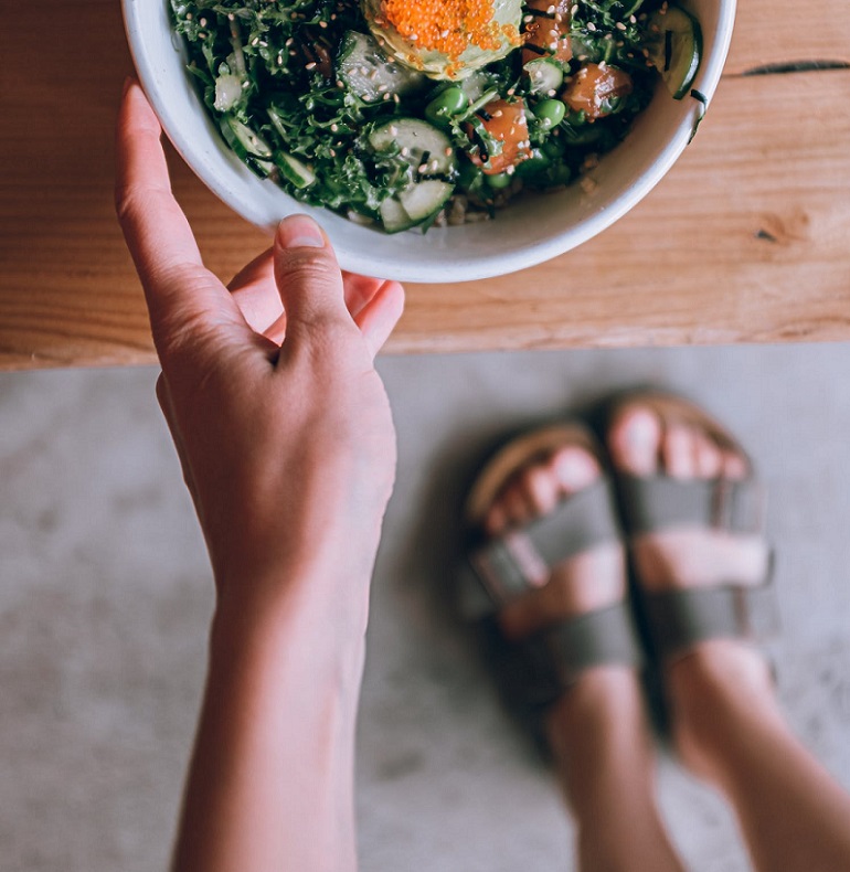 picture of person holding a bowl of salad, wearing slides on their feet 