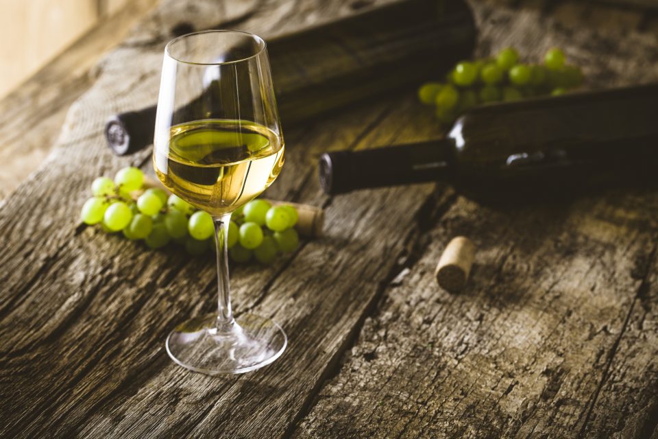 A glass of white wine with grapes beside it