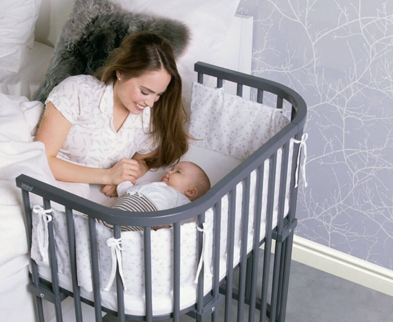 picture of a woman lying on a bedroom bed with a baby beside her in a co sleeper