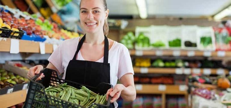 Blonde woman holding plastic basket with green beans in market blur background