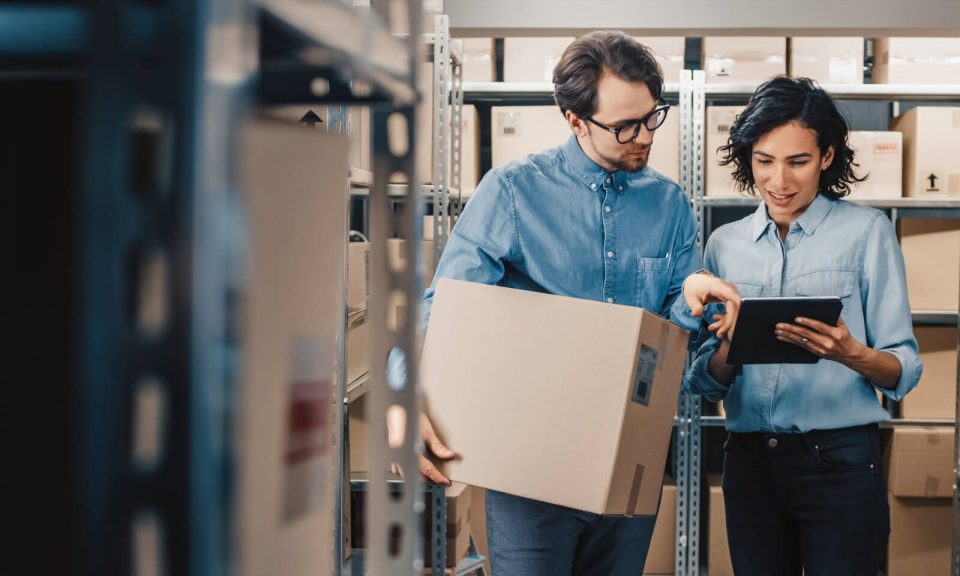 Woman with tablet and man with cartoon box talking in a warehouse