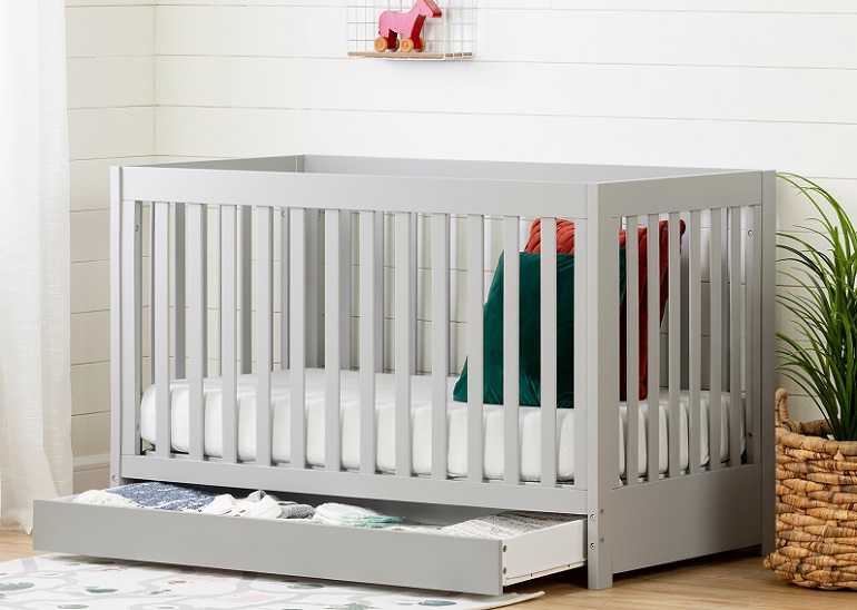 picture of a baby cot with ander crib drawer beside a plant 