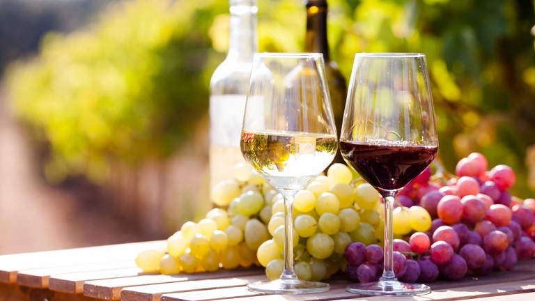 white and red wine and grapes on a table