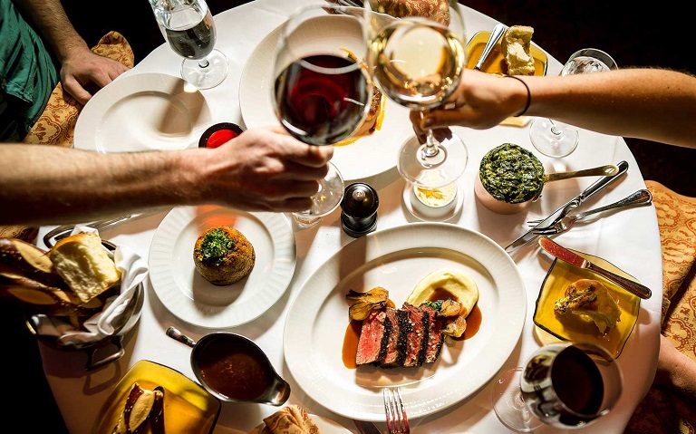 man and woman toasting with wine on the table full of food